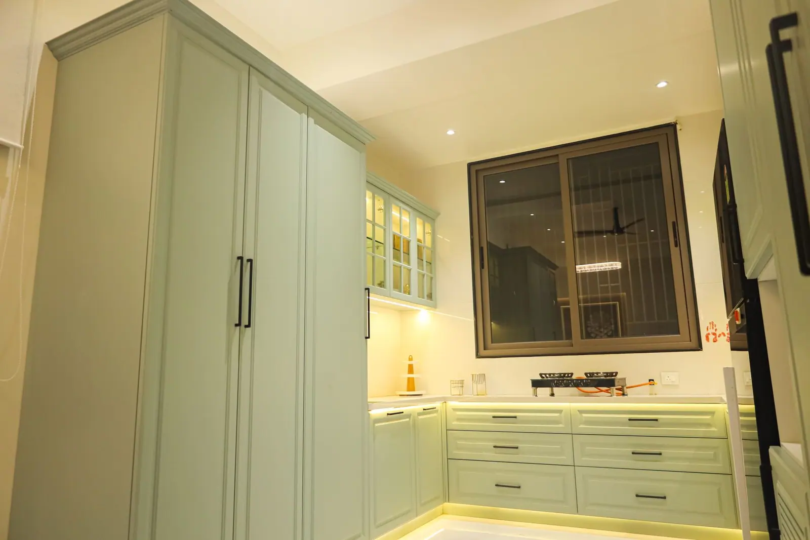 Utility corner — sage green shutters and drawers beside the window, next to a tall wardrobe.