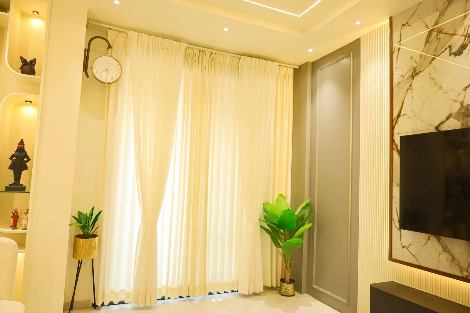 Living room — display niches, sheer drapes and a marble panel behind the television.