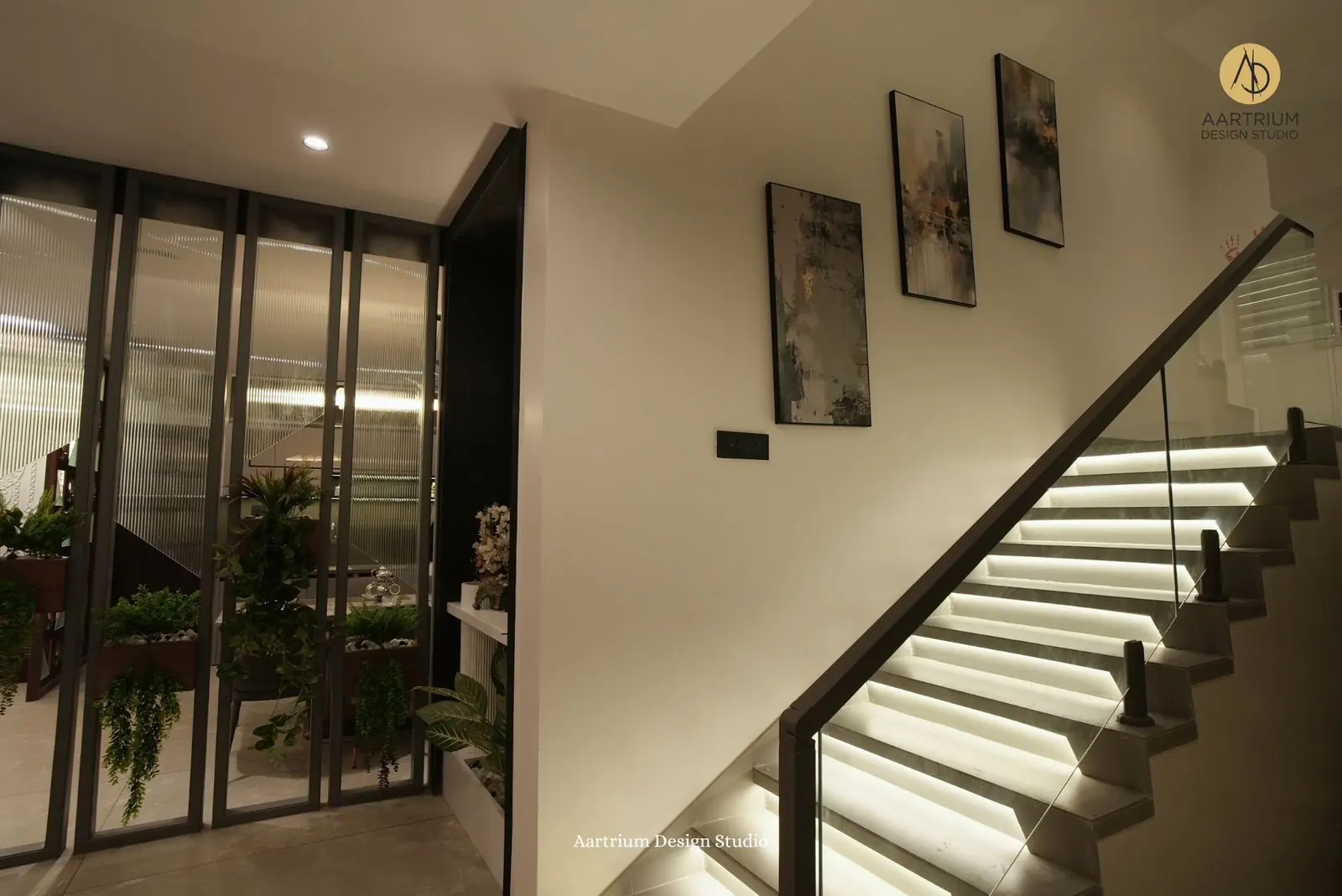 Staircase — a lit stone flight beside a full-height glazed screen and an art wall.